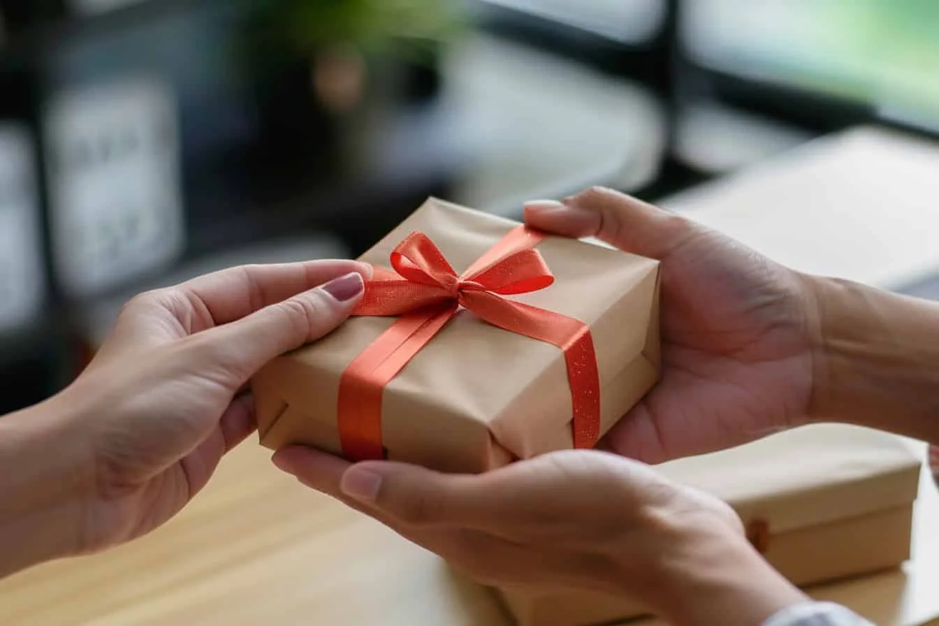 Hände übergeben ein sorgfältig verpacktes Geschenk an eine andere Person, symbolisiert eine Schenkung sowie eine mögliche Rückforderung wegen groben Undanks.